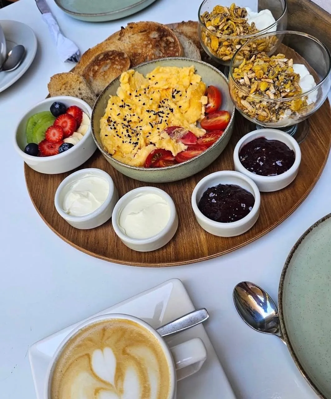 Tabla de brunch con huevos revueltos, tostadas, granola, frutas y café